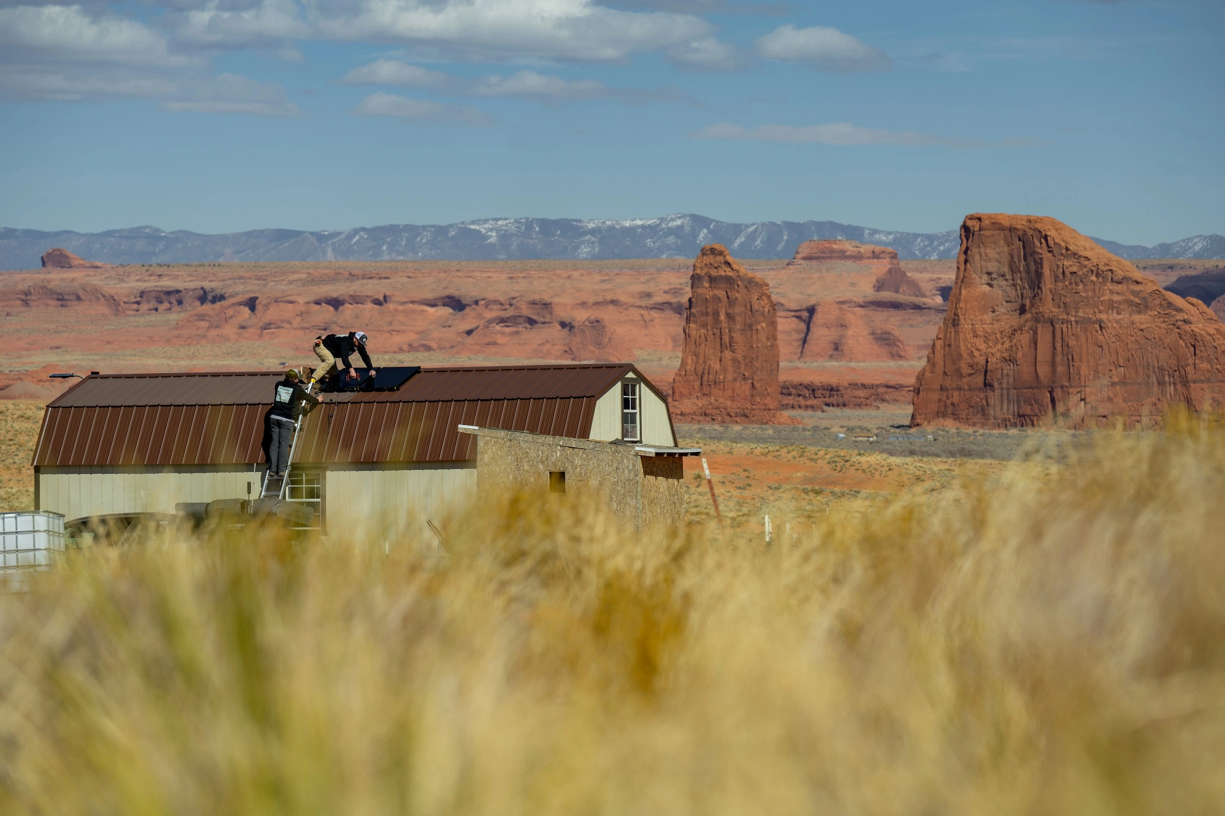 A view of a Navajoland desert landscape. Two men are perched on the roof of a large barn.